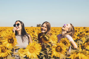 Three smiling girls wearing Nöz colored sunscreen on nose in field of sunflowers