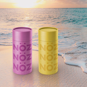 Up close view of Nöz Purple and yellow sunscreen bottles set by beach 